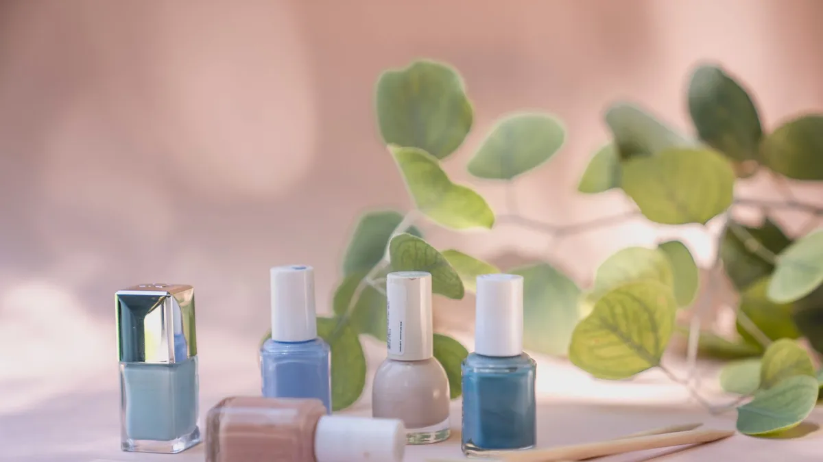 Các lọ sơn móng tay và cành lá trên nền hồng nhạt