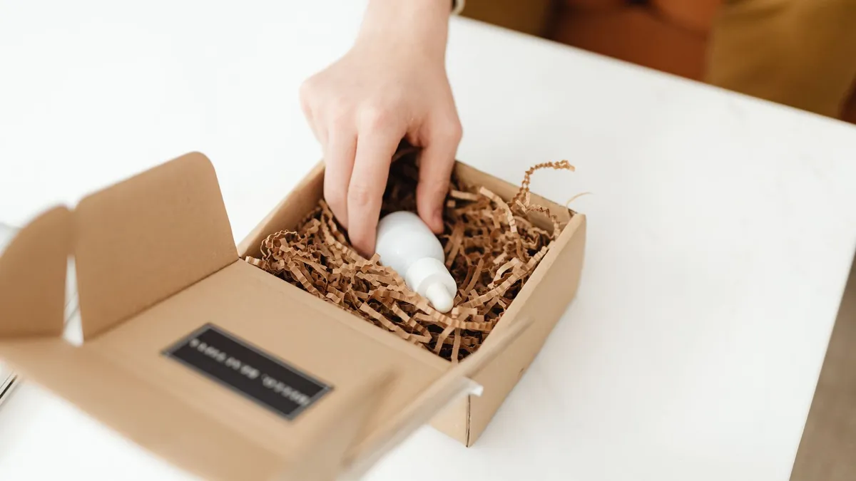 Tay đặt chai vào hộp carton có rơm giấy lót
